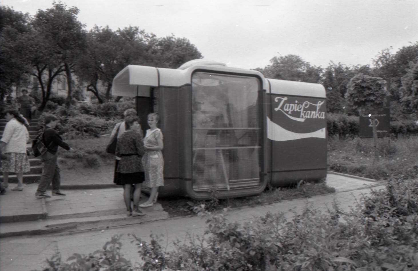Ludzie przy kiosku K67 z zapiekankami w parku - scena retro czarno-biała