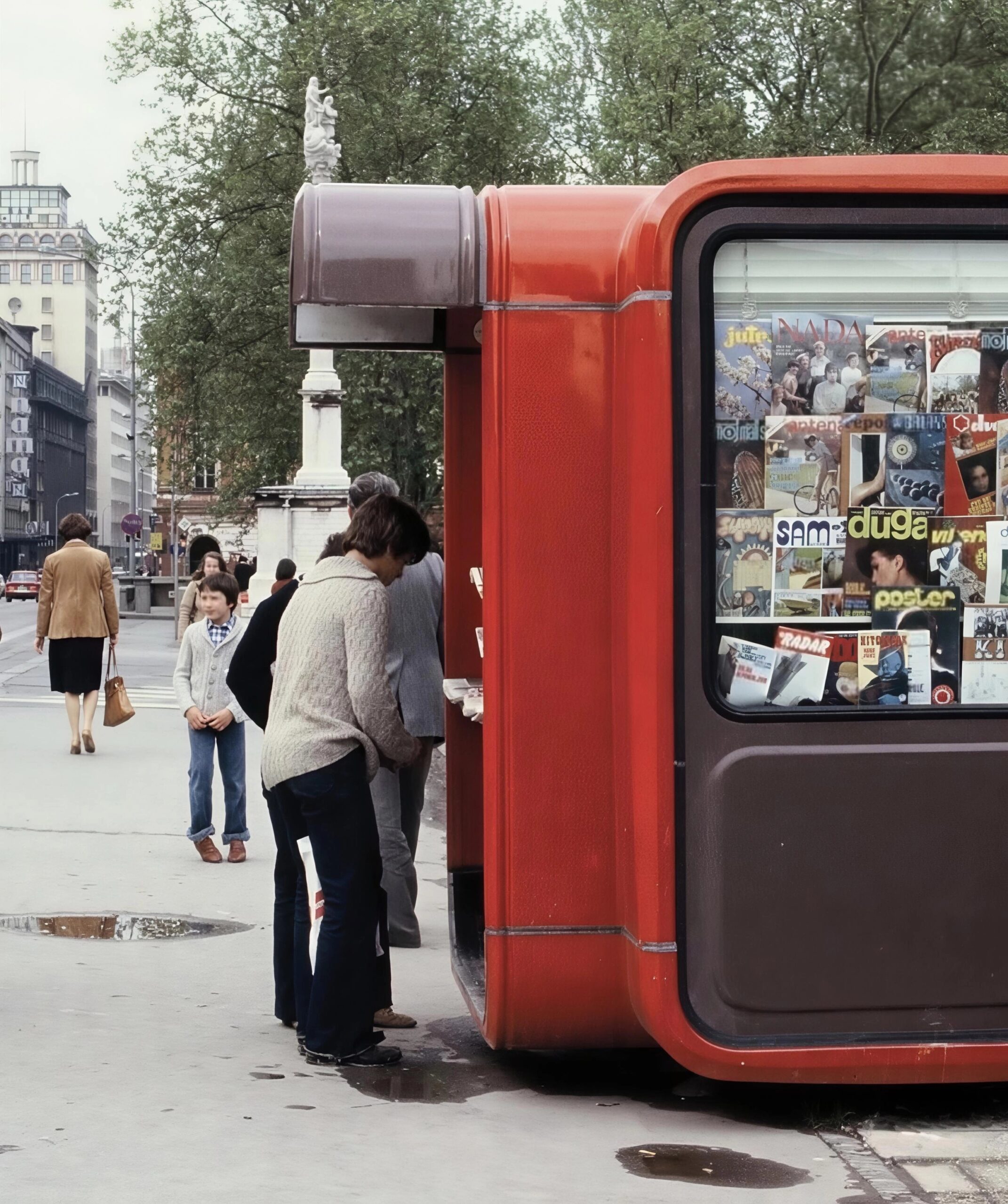 Ludzie przy czerwonym kiosku K67 z prasą na ulicy - scena retro